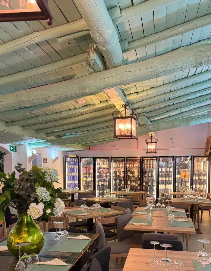 Sala del restaurante Los Pinochos en Simancas (Valladolid), con vigas pintadas en verde sage, faroles de forja y la vinoteca iluminada al fondo